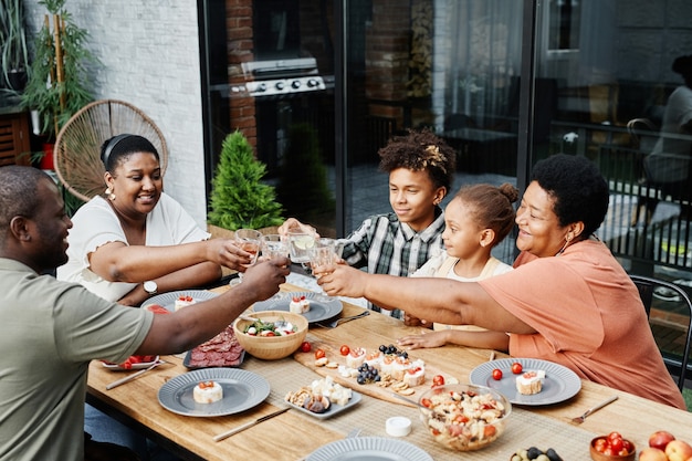 Retrato de gran familia afroamericana tintineando vasos mientras disfruta de una cena juntos al aire libre y ...