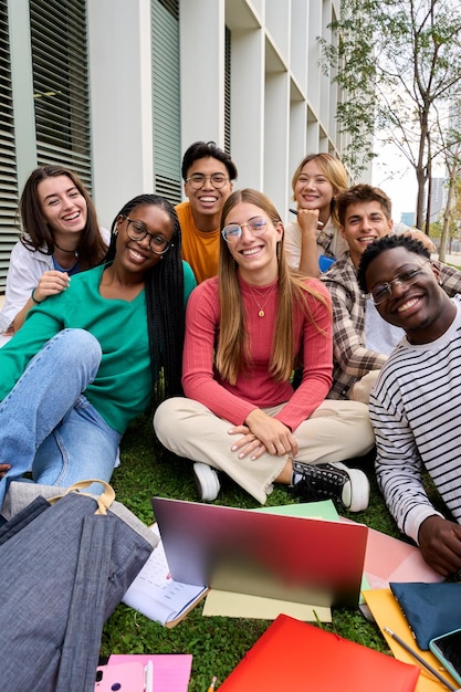 Retrato de un gran grupo de amigos multirraciales sentados posando sonriendo con una computadora portátil y cuadernos de trabajo