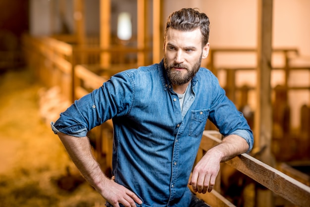 Retrato de un granjero empresario guapo de pie en el granero con cabras. Producción y cultivo de leche natural