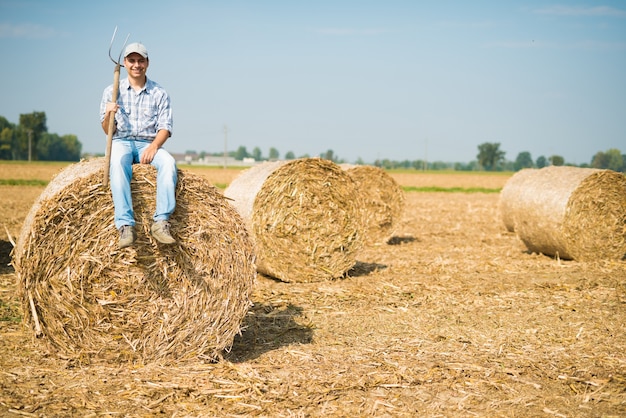 Retrato de un granjero sonriente que se sienta en un fardo de heno en su campo