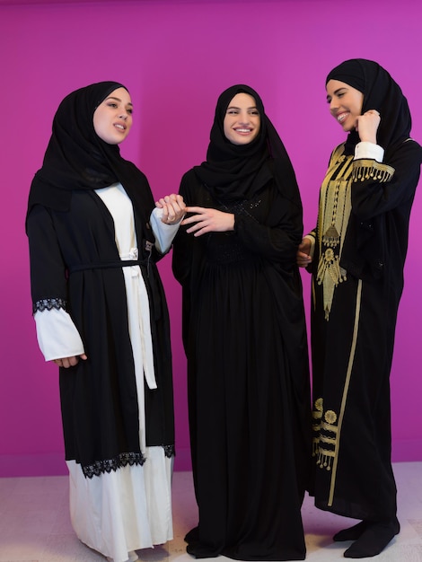 Retrato grupal de hermosas mujeres musulmanas, dos de ellas vestidas a la moda con hijab aisladas en un fondo rosado que representa la moda islámica moderna y el concepto de ramadán kareem.