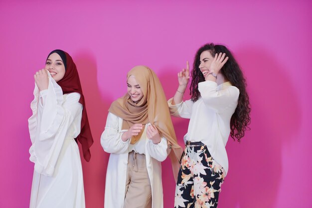 retrato grupal de hermosas mujeres musulmanas, dos de ellas vestidas a la moda con hiyab aisladas en un fondo rosado que representa la moda islámica moderna y el concepto ramadan kareem