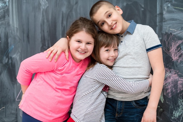 Foto retrato grupal de niños felices abrazándose mientras se divierten frente a una pizarra negra