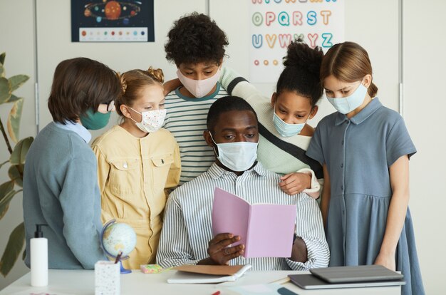 Retrato de un grupo diverso de niños y maestros con máscaras en el aula de la escuela, medidas de seguridad de covid