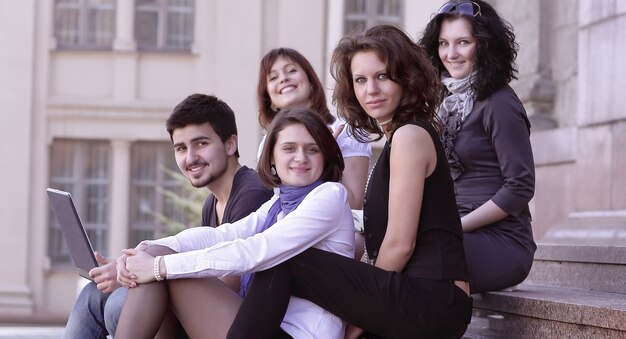 Retrato de un grupo de estudiantes sentados frente a la universidad