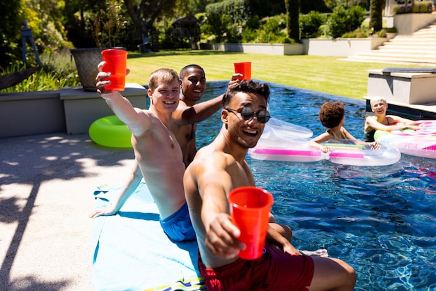 Retrato de un grupo feliz y diverso de amigos teniendo una fiesta en la piscina, sosteniendo vasos de plástico en el jardín. Estilo de vida, amistad, fiesta y verano.