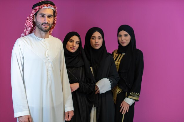 Retrato de grupo de jóvenes musulmanes hombres árabes con tres mujeres musulmanas en un vestido de moda con hiyab aislado sobre un fondo rosa.