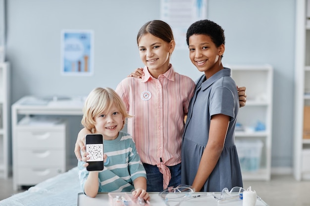 Foto retrato de un grupo de niños que muestran el código qr en la clínica de vacunación y sonríen a la cámara