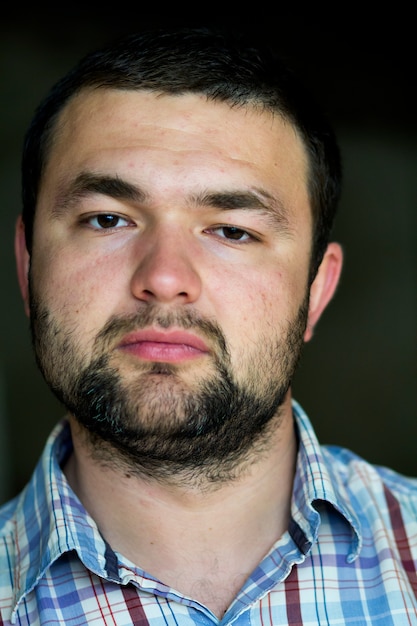 Foto retrato de guapo barbudo confiado inteligente joven moderno fotogénico joven con corte de pelo corto y amables ojos negros mirando cuidadosamente en cámara en gris