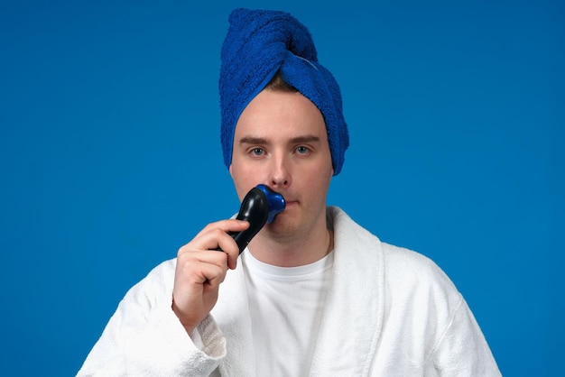 Retrato de guapo chico soñoliento joven se afeita la barba y el bigote de la cara con maquinilla de afeitar eléctrica