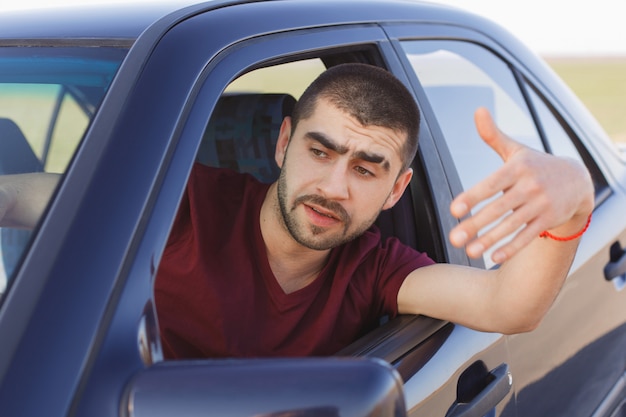 Retrato de guapo conductor masculino olas desde la ventana del coche