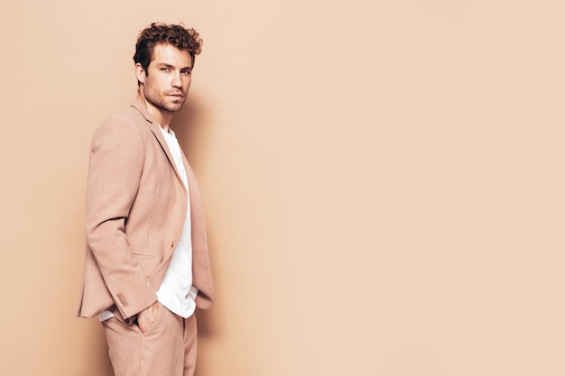 Retrato de guapo confiado con estilo hipster lambersexual modelo Sexy moderno hombre vestido con elegante traje beige Moda hombre con peinado rizado posando en estudio aislado
