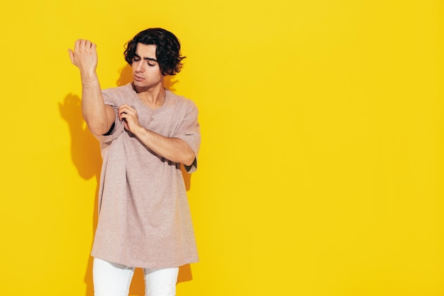 Retrato de guapo confiado con estilo hipster lambersexual modelSexy hombre vestido con camiseta de gran tamaño y jeans Hombre de moda aislado en el estudio Posando cerca de la pared amarilla