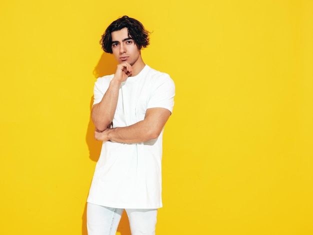 Retrato de guapo confiado con estilo hipster lambersexual modelSexy hombre vestido con camiseta de gran tamaño y jeans Hombre de moda aislado en el estudio Posando cerca de la pared amarilla
