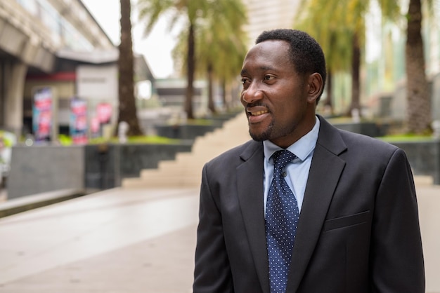 Retrato de guapo empresario africano en la ciudad sonriendo y pensando