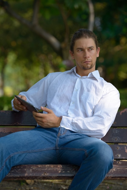 Retrato de guapo empresario barbudo con cabello largo relajándose en el parque al aire libre