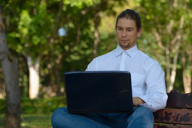 Retrato de guapo empresario barbudo con cabello largo relajándose en el parque al aire libre