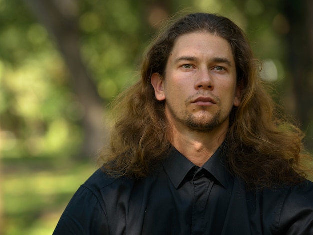 Retrato de guapo empresario barbudo con cabello largo relajándose en el parque al aire libre