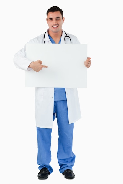 Retrato de un guapo médico apuntando a un panel en blanco