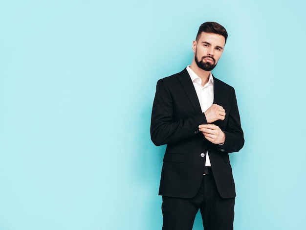 Retrato de guapo modelo lambersexual con estilo hipster con estilo Sexy hombre moderno vestido con elegante traje negro Hombre de moda posando en el estudio cerca de la pared azul