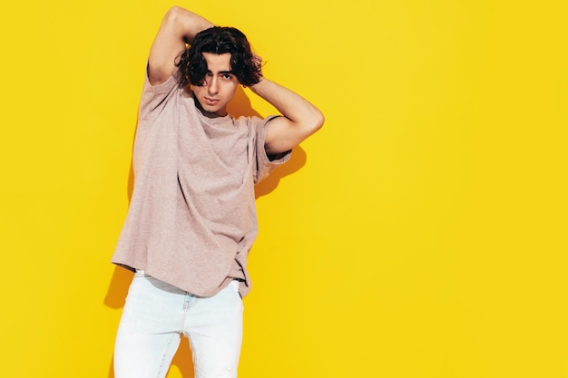 Retrato de guapo modelo lambersexual hipster con estilo seguro Hombre vestido con camiseta de gran tamaño y jeans Hombre de moda aislado en el estudio Posando cerca de la pared amarilla