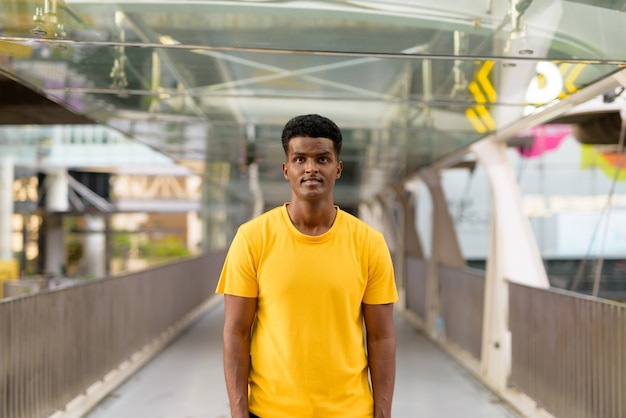 Retrato de guapo negro africano hombre vestido con camiseta amarilla al aire libre en la ciudad de Bangkok, Tailandia