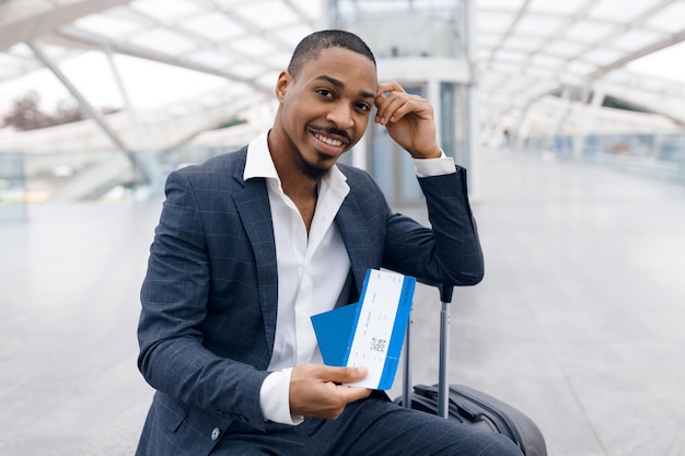 retrato, de, guapo, negro, hombre de negocios, con, pasaporte, y, boletos aéreos, en, mano