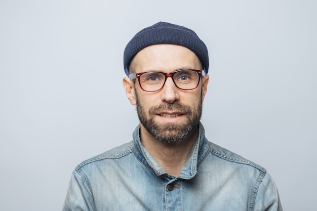 Retrato de guapo periodista masculino elegante usa gafas, sombrero de moda y chaqueta vaquera