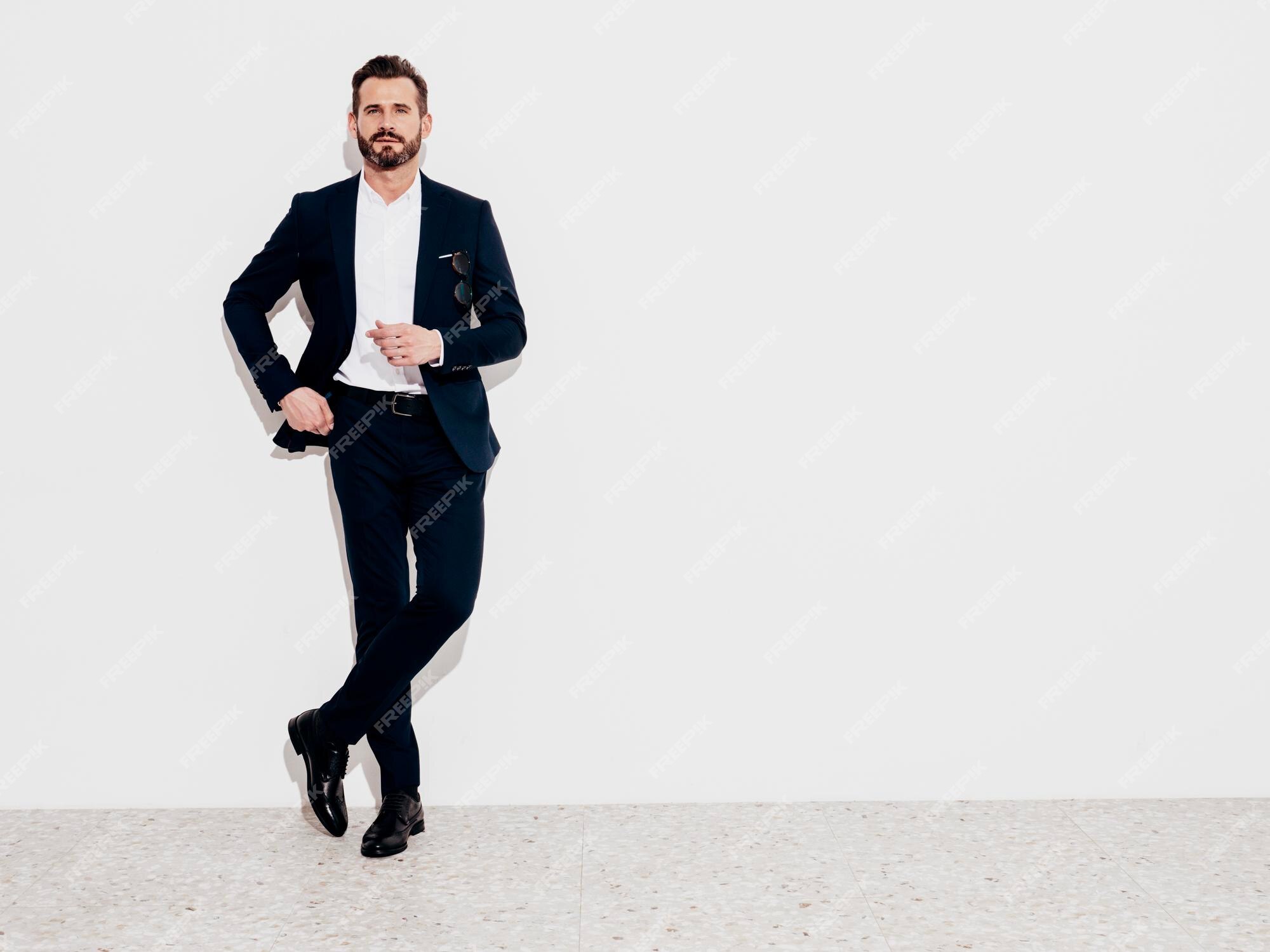 Retrato de guapo sonriente elegante modelo hipster hombre moderno sexy vestido con traje negro elegante hombre de moda posando en el estudio cerca de la pared blanca longitud total | Foto Premium