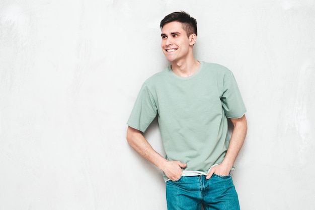 Retrato de guapo sonriente con estilo hipster lambersexual modelMan vestido con camiseta y jeans Hombre de moda aislado en el estudio Posando cerca de la pared gris Alegre y feliz