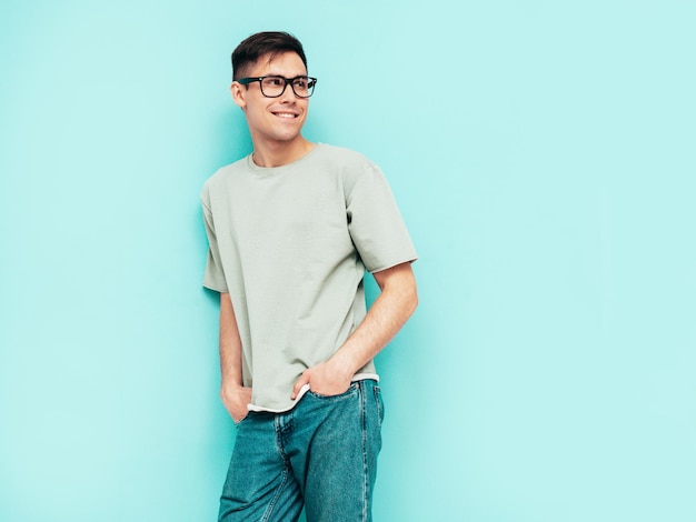 Retrato de guapo sonriente con estilo hipster lambersexual modelo Hombre vestido con camiseta y jeans Moda hombre aislado en estudio Posando cerca de la pared azul Alegre y feliz