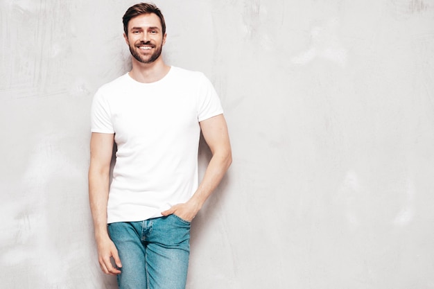 Retrato de guapo sonriente con estilo hipster lambersexual modelo Sexy hombre vestido con camiseta y jeans Moda hombre aislado en la pared azul en el estudio
