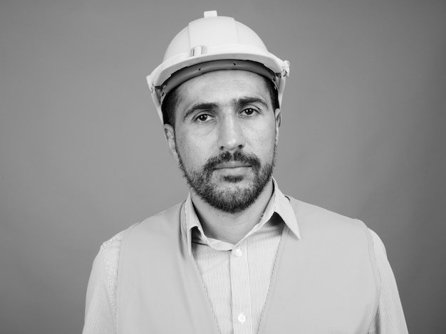 Retrato de guapo trabajador de la construcción persa barbudo en gris en blanco y negro