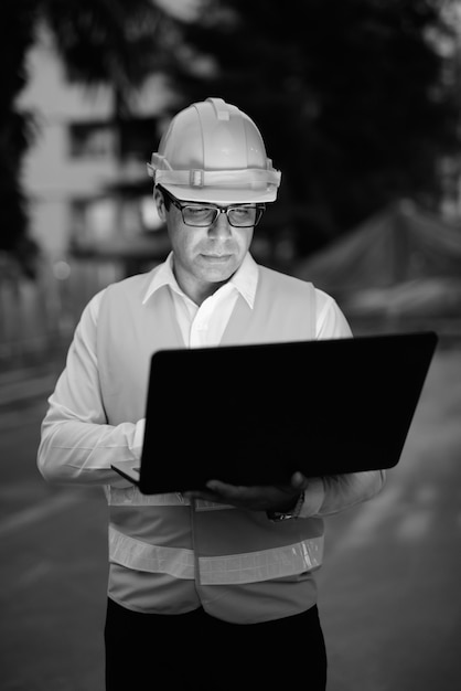 Retrato de guapo trabajador de la construcción persa en el sitio de construcción en blanco y negro