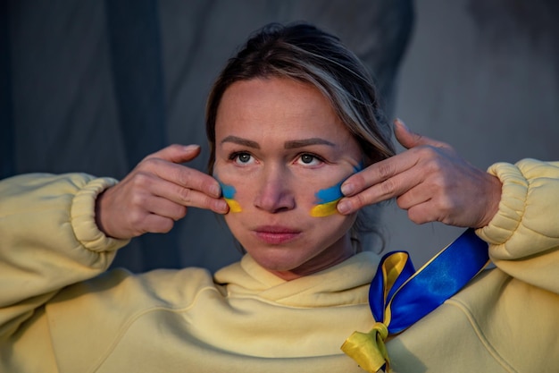 Retrato de guerra de mujer ucraniana con bandera nacional en la mejilla llorando