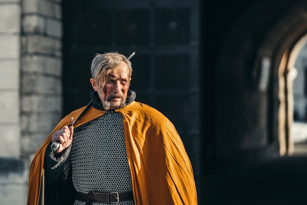 Retrato de un guerrero medieval con armadura después de una batalla con sangre en su rostro. El guerrero sostiene la espada en sus manos.