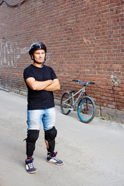 Retrato de guy rider de pie junto a la bicicleta en el callejón del edificio de ladrillo rojo