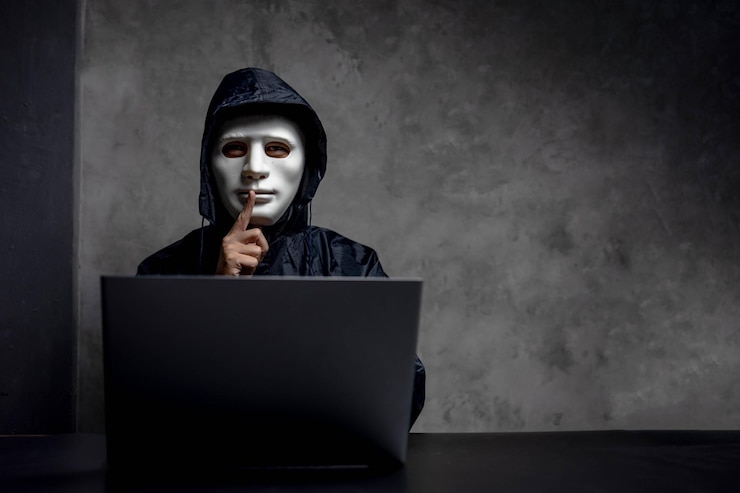 Foto retrato de un hacker informático con el dedo en los labios sentado junto a una computadora portátil en la mesa contra la pared