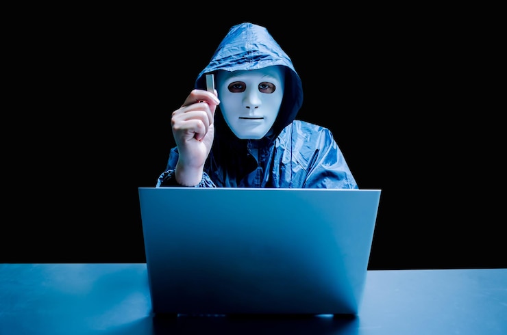 Foto retrato de un hacker masculino con una máscara mientras muestra una pinza usb con una computadora portátil en la mesa contra un fondo negro