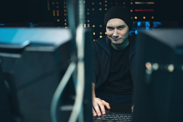 Retrato de un hacker sonriente con una sudadera y una gorra que intenta hackear un sistema de seguridad