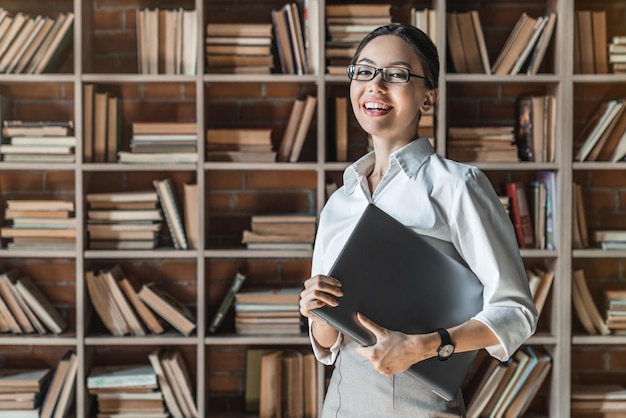 retrato, de, hembra joven, con, computador portatil, en, biblioteca