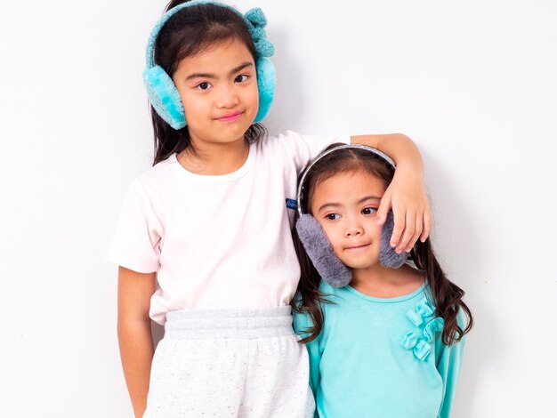 Retrato de hermanas sonrientes con tapones para las orejas de pie contra un fondo blanco