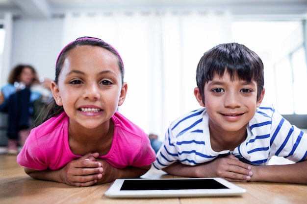 Retrato de hermano y hermana acostada en el piso con tableta digital