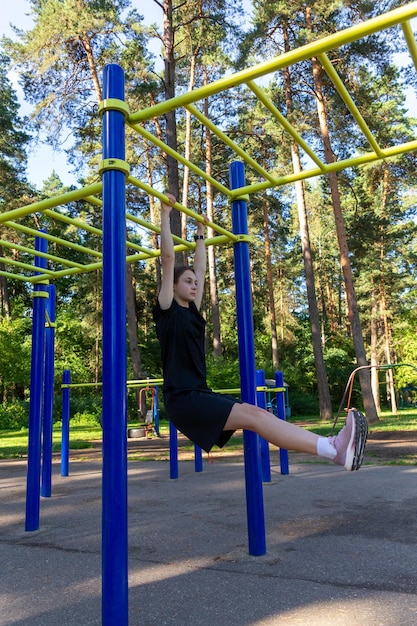 Retrato de una hermosa adolescente atlética entrenando al aire libre en un gimnasio al aire libre en un día soleado de verano gana músculos abdominales en una barra horizontal fitness estilo de vida saludable