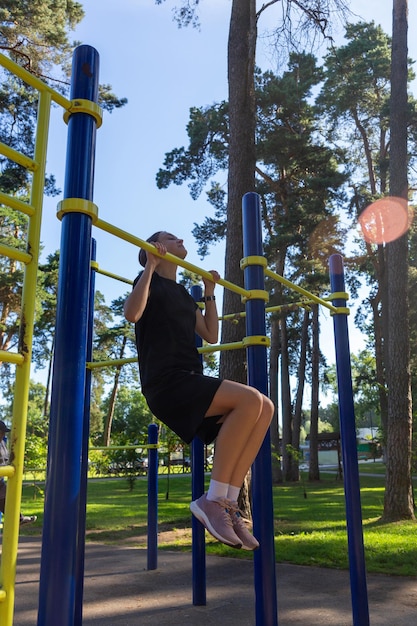 Foto retrato de una hermosa adolescente atlética entrenando al aire libre en un gimnasio al aire libre en un día soleado de verano para ganar músculos de las manos en la barra horizontal fitness estilo de vida saludable