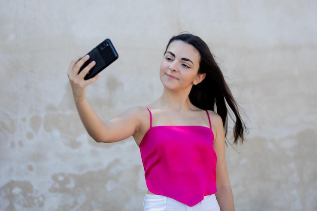 Retrato de una hermosa adolescente de cabello oscuro con top rosa mirando su teléfono móvil