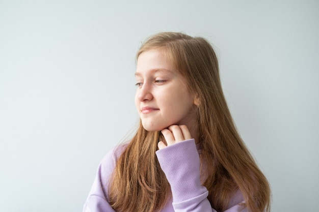 Retrato de una hermosa adolescente con el pelo largo en morado con capucha de pie contra la pared blanca.