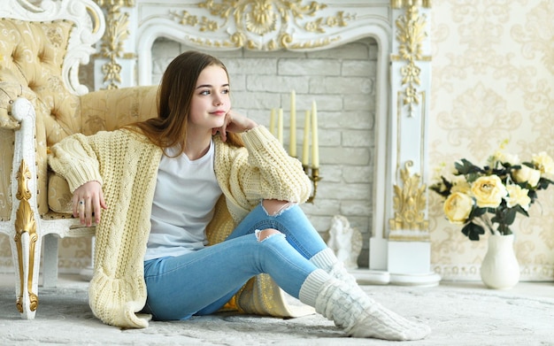 Retrato de una hermosa adolescente sentada en el suelo cerca de un sillón antiguo