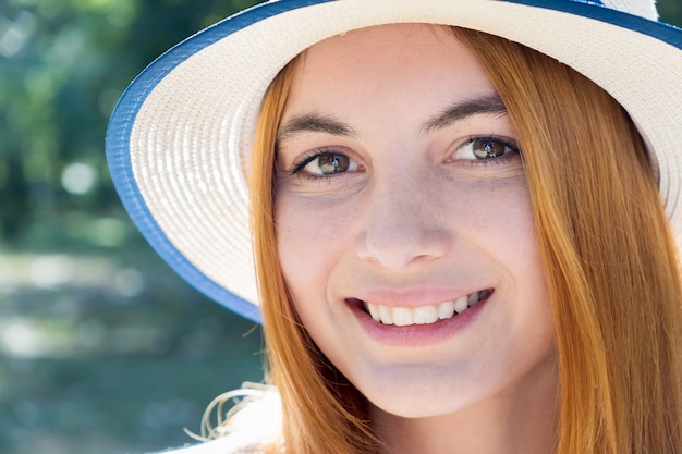 Retrato de hermosa adolescente sonriente con sombrero amarillo y con el pelo rojo al aire libre en un día soleado de verano.