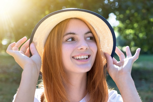 Retrato de hermosa adolescente sonriente con sombrero amarillo y con el pelo rojo al aire libre en un día soleado de verano.